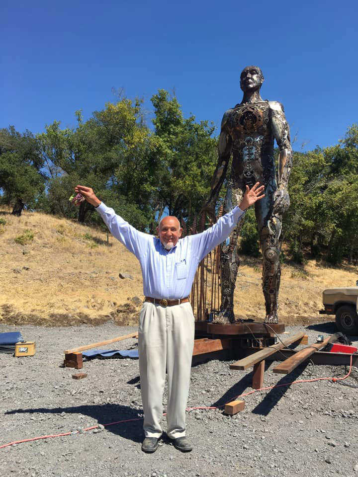 Dr. Walter Byck with arms open in sculpture garden